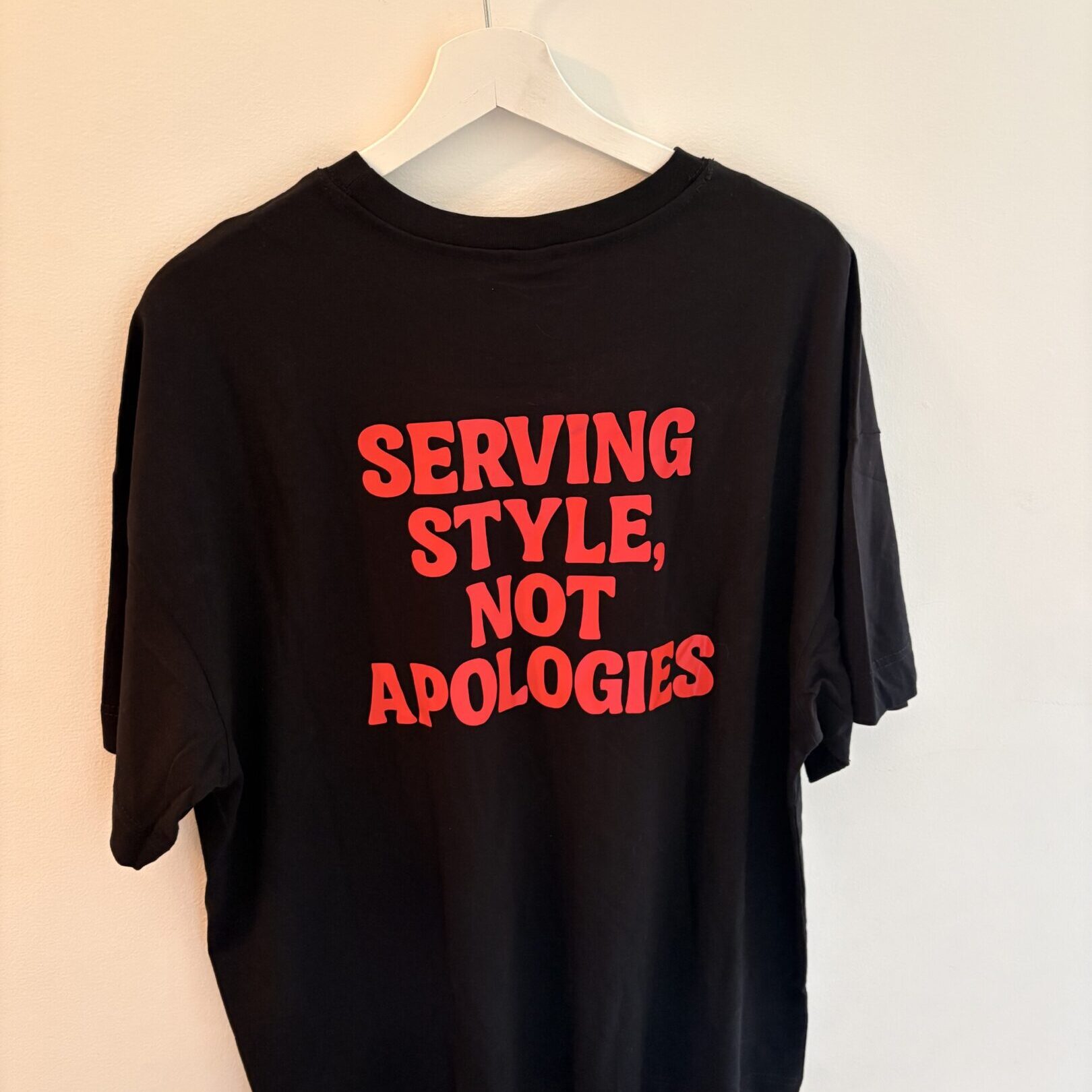 Black T-shirt with bold red text saying 'SERVING STYLE, NOT APOLOGIES'.